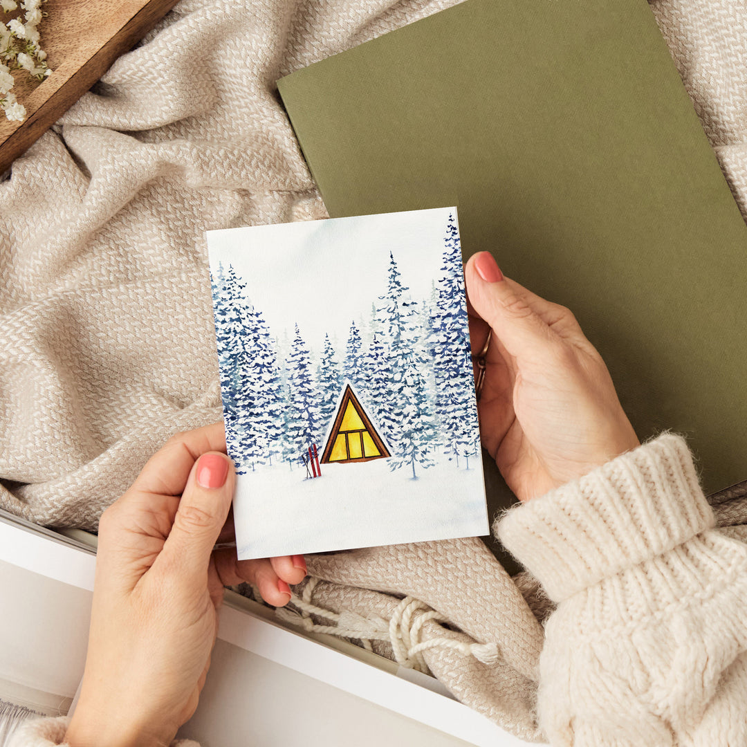a person holding a card with a picture of a cabin in the woods