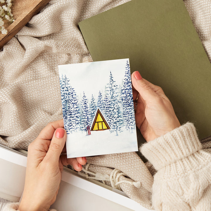 a person holding a card with a picture of a cabin in the woods