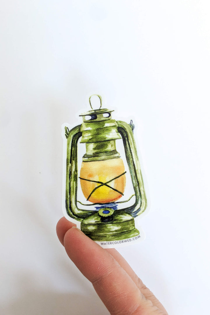 a hand holding a small green lantern ornament