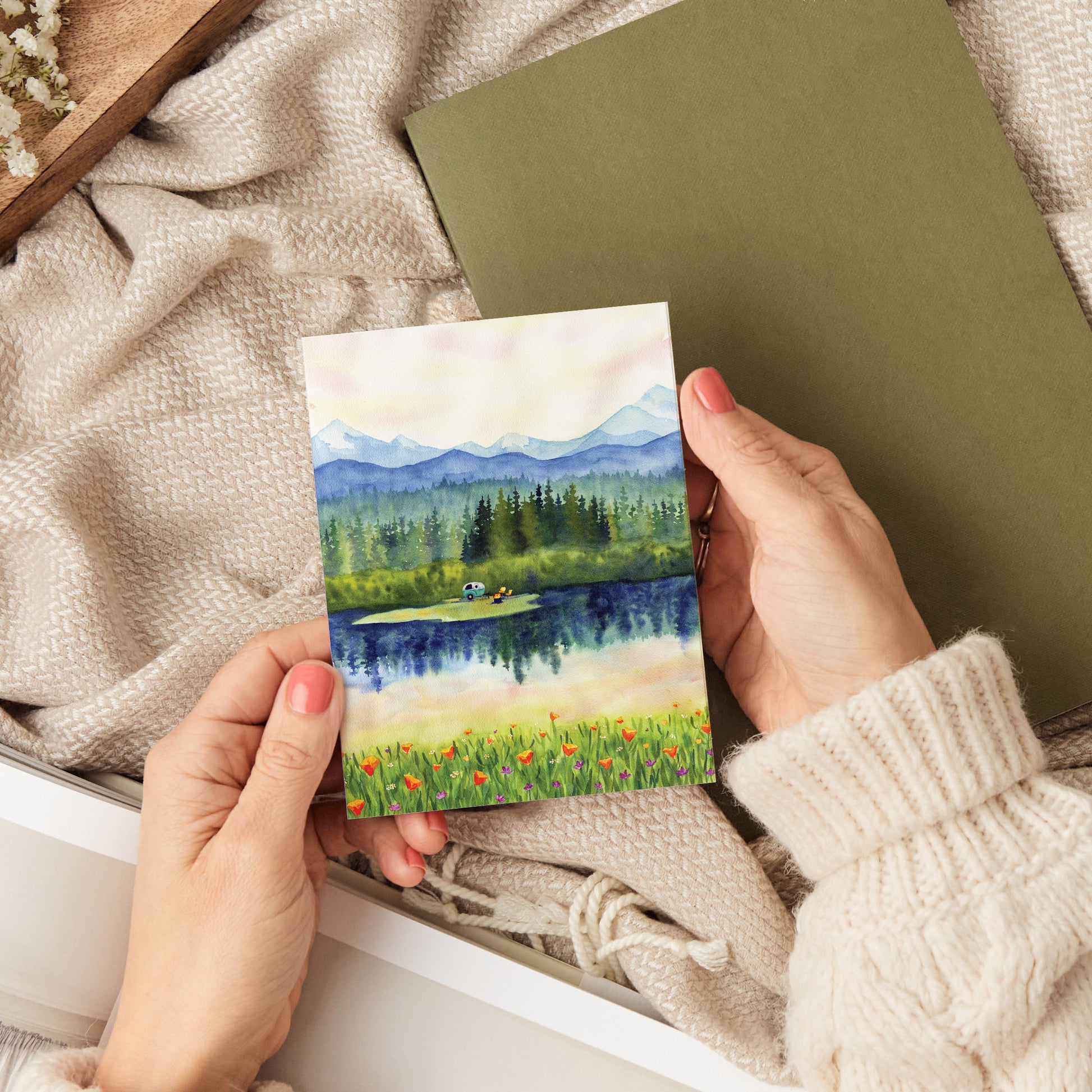 a person holding a card with a lake scene painting on it