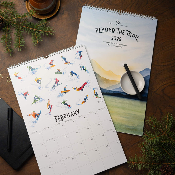 Two calendars on a wooden surface with a pen and decorative elements.