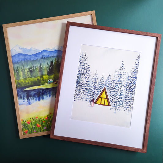 two paintings of trees and an aframe cabin both in wood frames