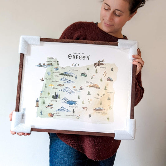 a woman holding a framed map of oregon