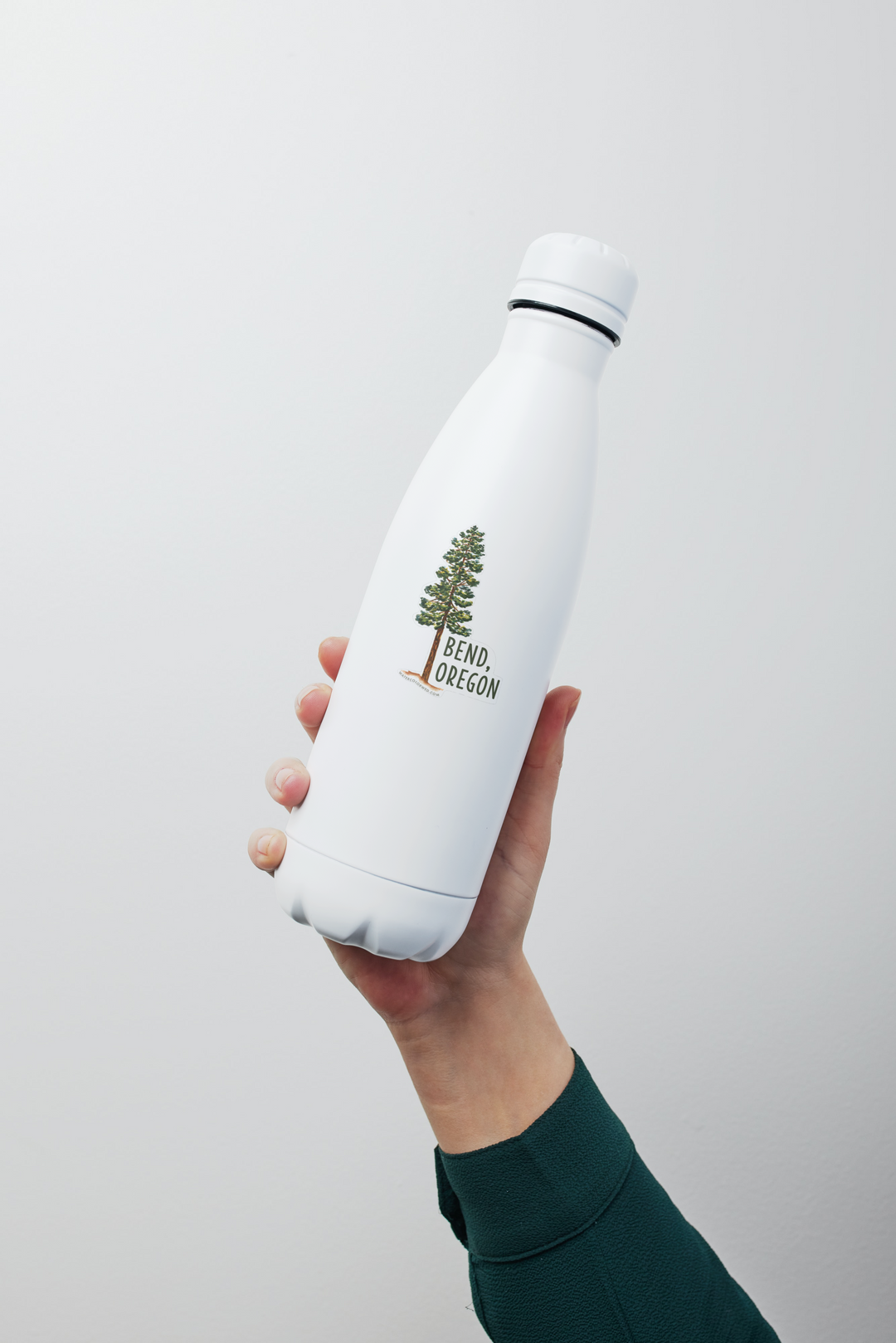 a person holding a white water bottle in their hand with a pine tree sticker